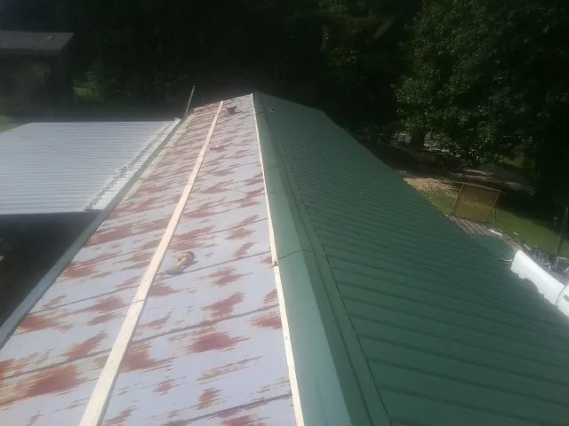 Old rusted panels beside newly installed green metal roofing — Wind Damage Roof Repair by Roofing Brothers in Imperial